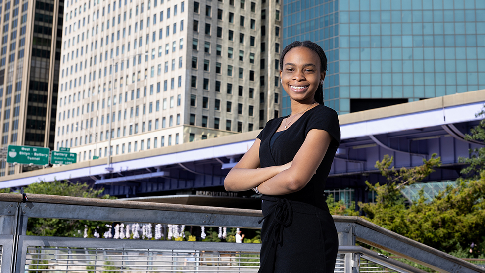 Candice Garwood stands on a pedestrian bridge with a city skyline behind her.